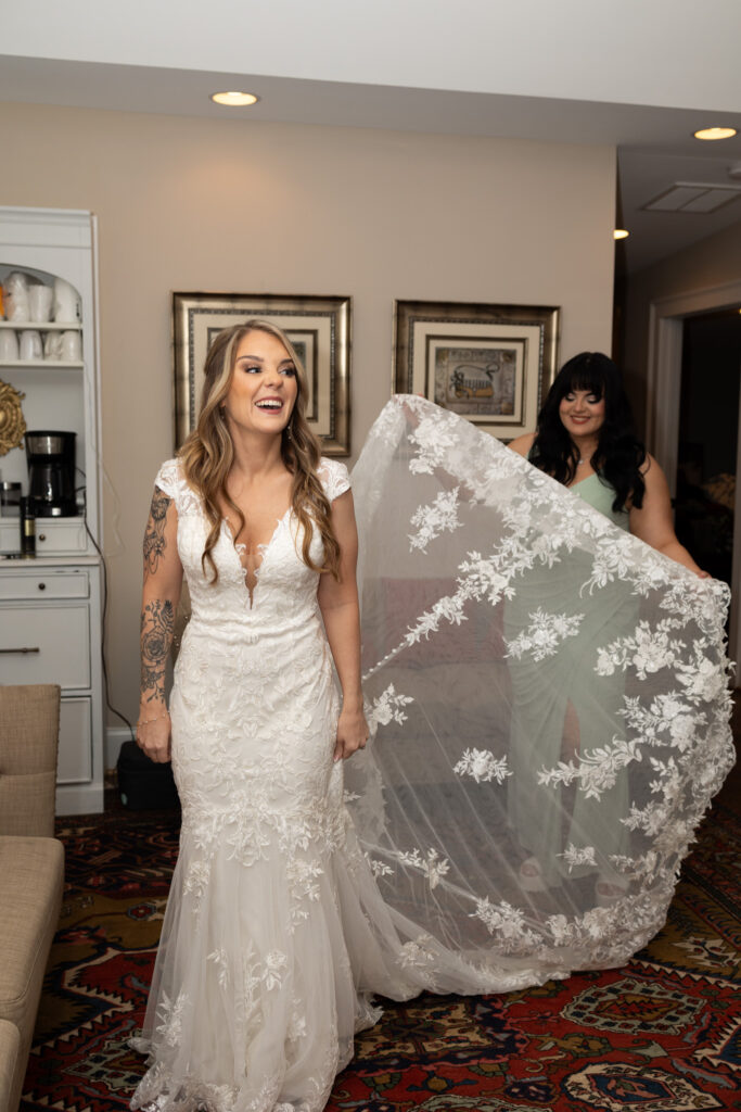 Bride's sister holding wedding dress for portrait while both women smile at the camera in the bridal getting ready suite