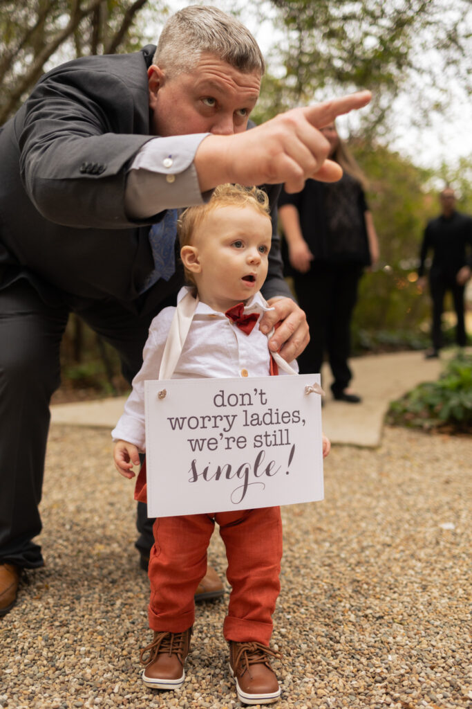 Child at a wedding wearing a sign that says "don't worry ladies, we're still single!"