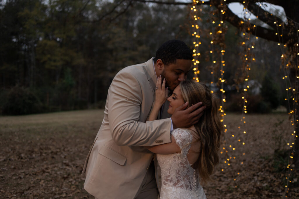 Groom kisses side of bride's temple during couple's portraits in Monroe, GA