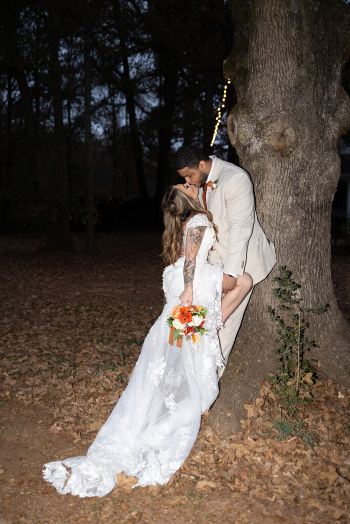 Spicy wedding couple's photos. Bride kisses groom against tree, flash photo, Monroe, GA